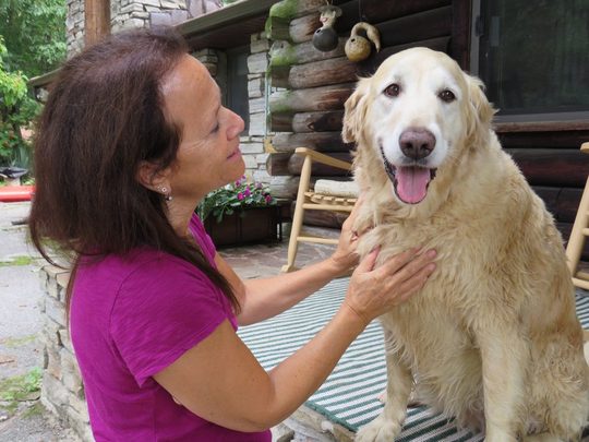 Donna Sue Rosenthal kneeling on a porch, greeting an older golden retriever